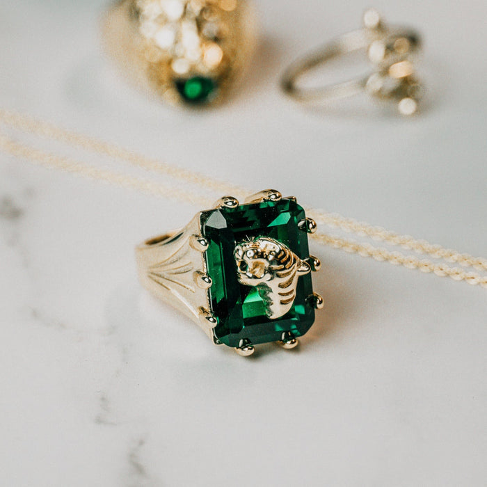 Gold ring with a large emerald stone on a marble surface