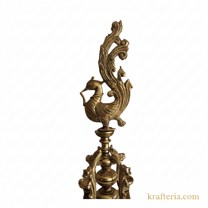 A brass peacock diya with four wicks on a pedestal.