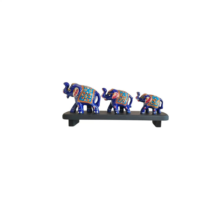Three hand-painted blue elephant figurines of varying sizes, decorated with colorful traditional patterns, displayed on a dark grey stand.