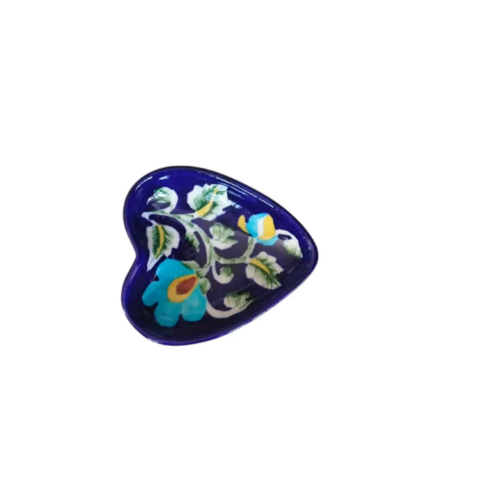 A small, heart-shaped blue pottery soap dish with intricate hand-painted light blue and yellow floral designs and green leaves, sitting on a light-colored tiled surface.